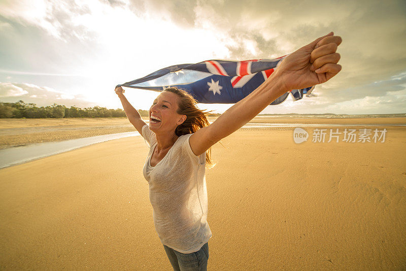 日落时分，沙滩上的白人女性举着澳大利亚国旗