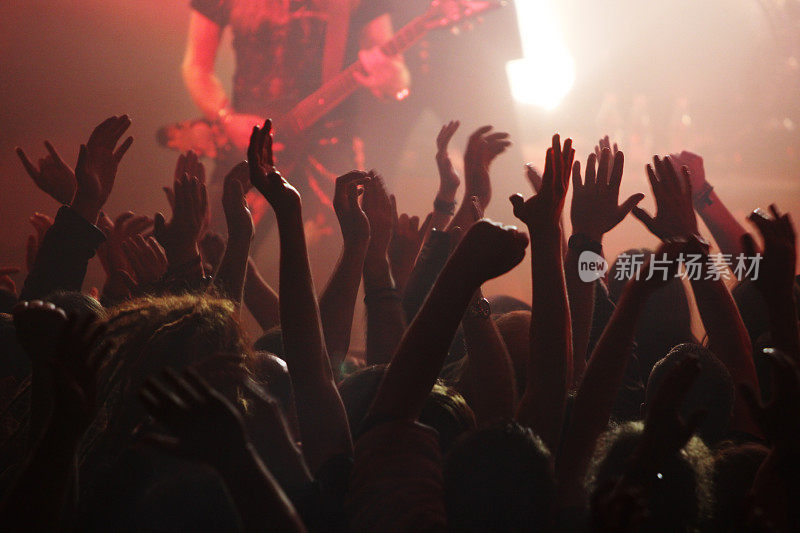 在一场有红色灯光的摇滚音乐会上，人们举起手臂