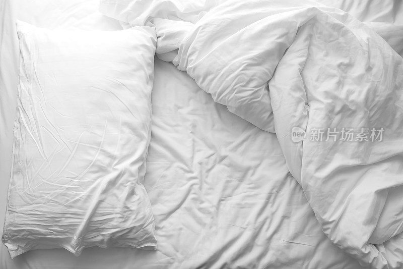 凌乱的床上。床上的白色枕头和毛毯未整理。早晨过后放松的概念。