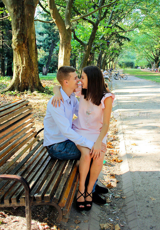 一对年轻夫妇坐在公园的木凳上，拥抱亲吻
