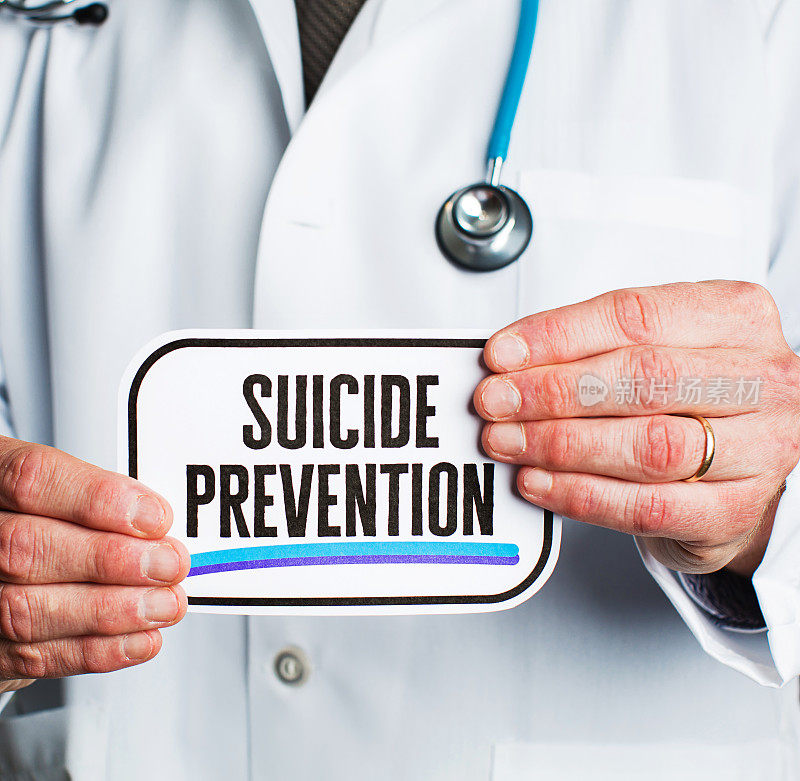 戴着听诊器的医生穿着白大褂，手里举着写着“预防自杀”的牌子