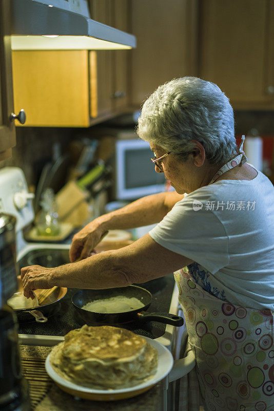 70岁高龄的银发老奶奶正在厨房里做煎饼当早餐。