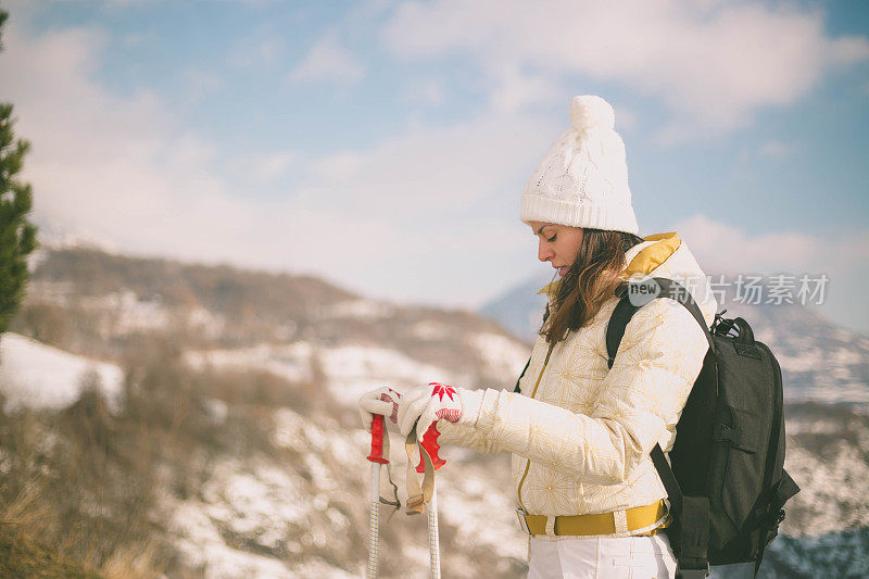 近景美丽的年轻女子在冬天的衣服站在一边，手拿木棍的背景雪山