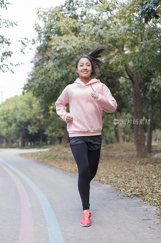 年轻女子在柏油路上伴着音乐奔跑