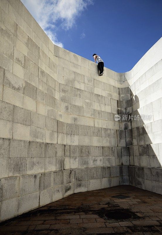 一个年轻人正在爬一堵巨大的混凝土墙