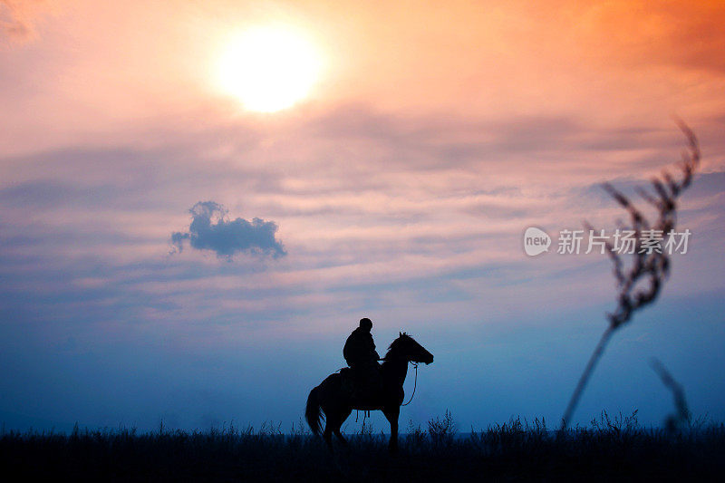 哈萨克斯坦，一名骑在马背上的骑手在五彩缤纷的夕阳中