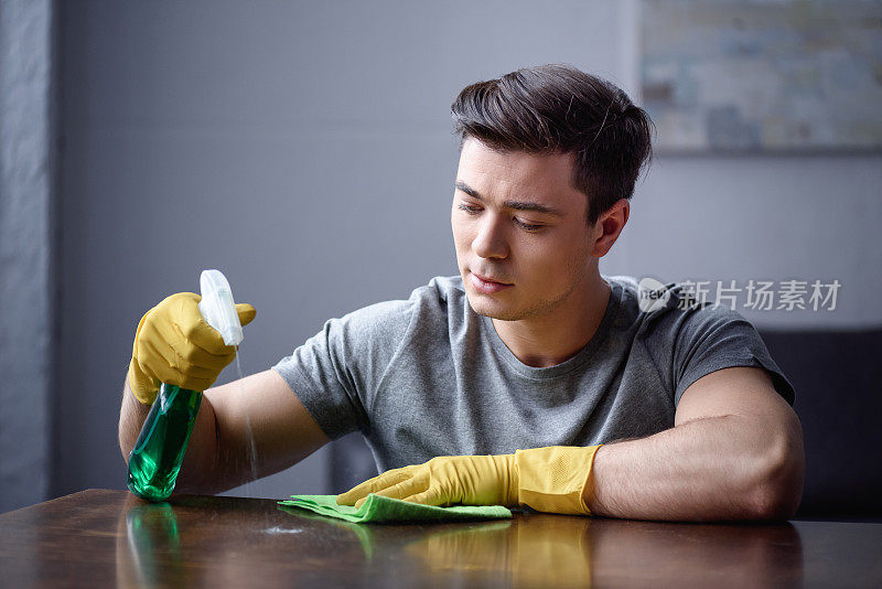 一个男人正在用喷瓶和抹布清洁客厅的桌子