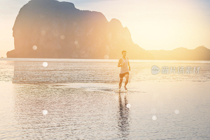 年轻的亚洲男子在海滩上奔跑，夕阳为背景