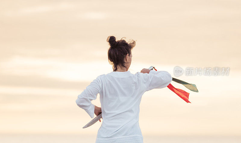 女子面朝夕阳，练习吴式佩刀式太极拳