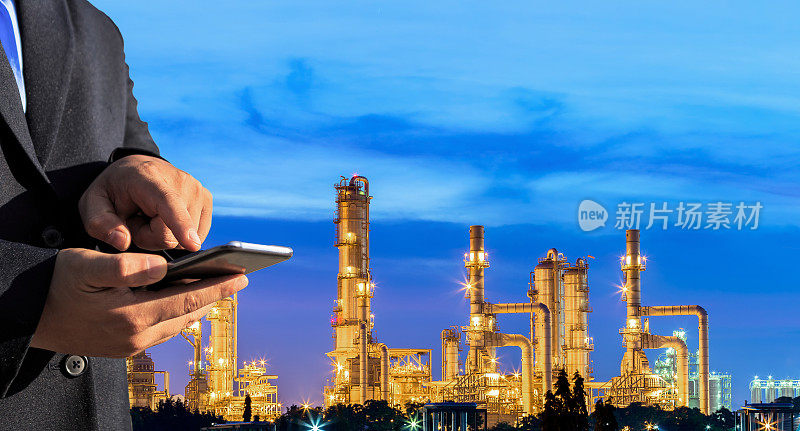 作为能源和技术的概念，商人在晚上用智能手机检查炼油厂工厂