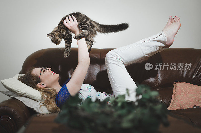 一个女人坐在沙发上和一只猫玩