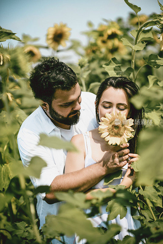 一对年轻的成年夫妇在一个阳光明媚的日子里闻着向日葵