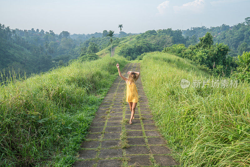 开朗的女性穿着黄色的裙子走在绿色的米上，走在巴厘岛的乌布，快乐的人旅行目的地自由奇妙的理念
