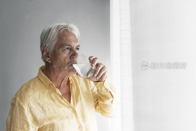 窗边沉思的老人拿着一杯水的照片