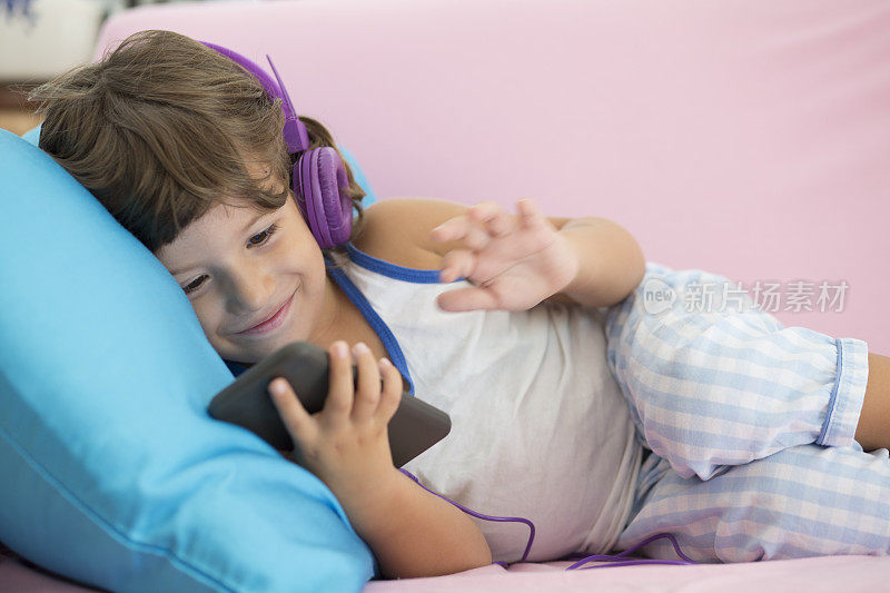 快乐的小男孩在家里用智能手机和耳机