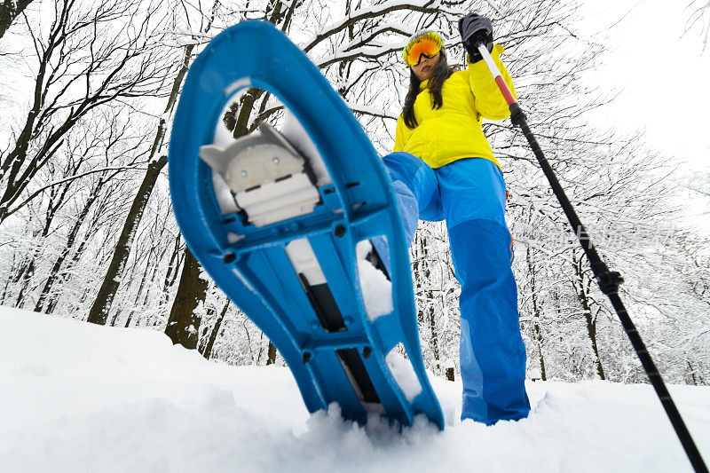 徒步登山的人用她的雪鞋和手杖在厚厚的积雪中大步行走