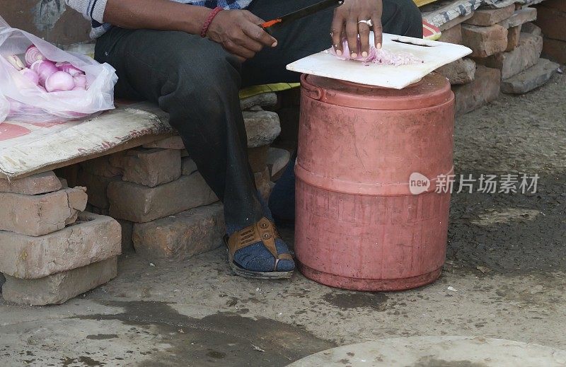图为一名印度男子在印度德里市场的街头小吃摊上切红洋葱