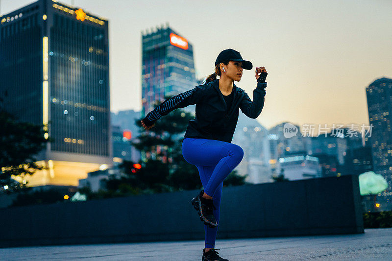 自信年轻的运动女性锻炼和伸展户外对城市景观在日落