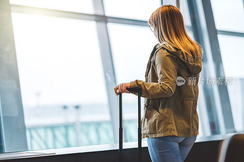 拿着行李箱的女人从机场的窗户往外看