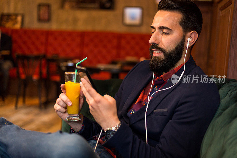 放松的胡子男人使用智能手机和喝