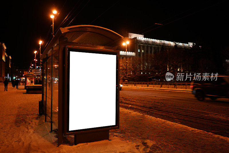 垂直广告牌在冬天的公交车站。公交车站在晚上的城市。广告设计模型与白色的领域。
