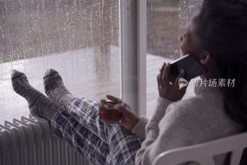 女人休息，用智能手机聊天，喝茶，在家取暖。