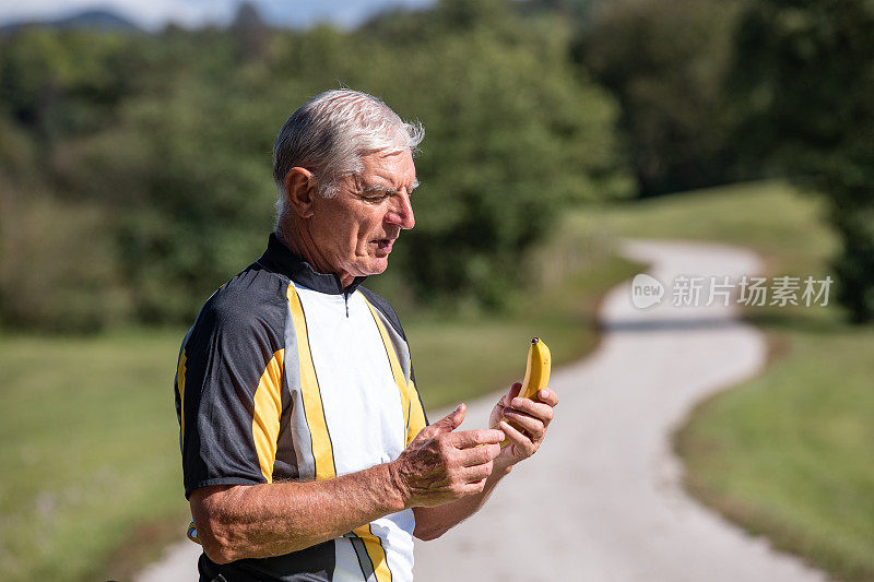 活跃的老年自行车手拿着香蕉站在乡村公路上