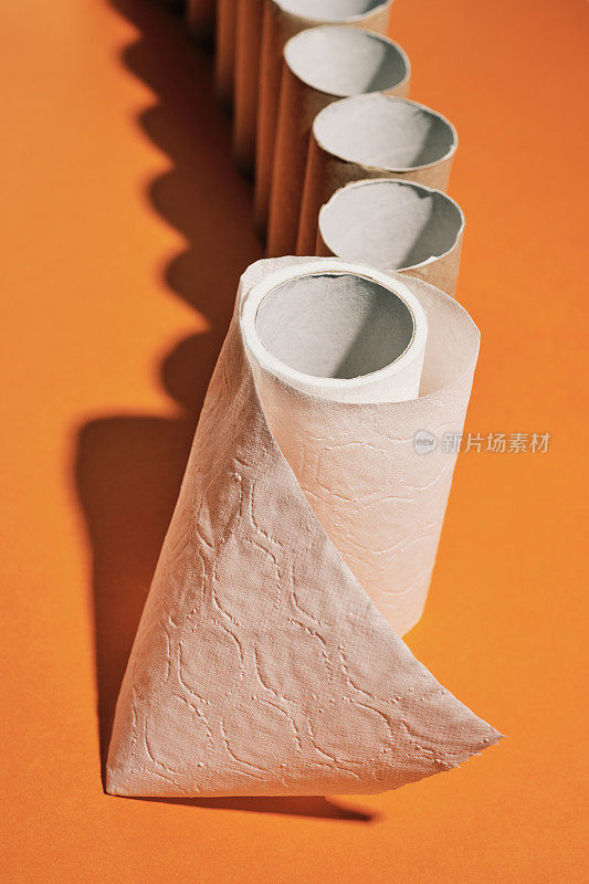 在明亮的橙色背景下，几乎空无一物的厕纸在一排空厕纸的前面。