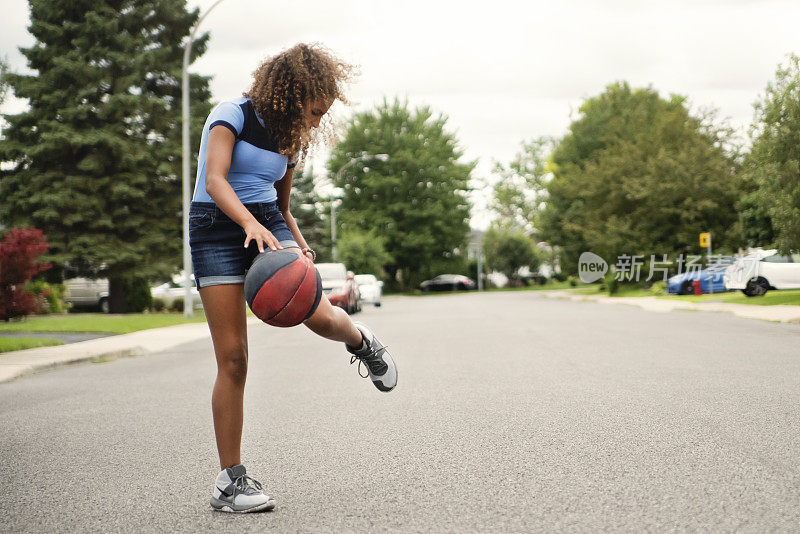 混血少女在郊区街道练习篮球。