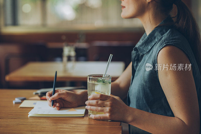 一个女人喝柠檬水和写在她的笔记本在咖啡馆的特写