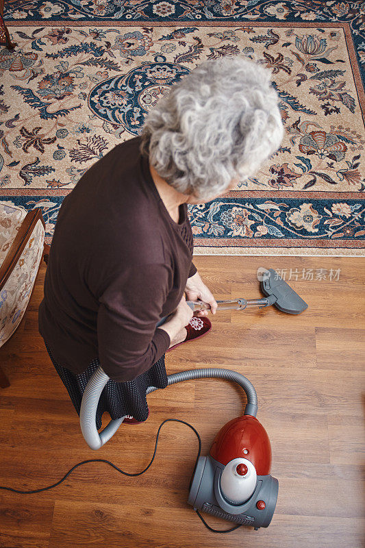 穿着便服的老妇人用吸尘器打扫房子
