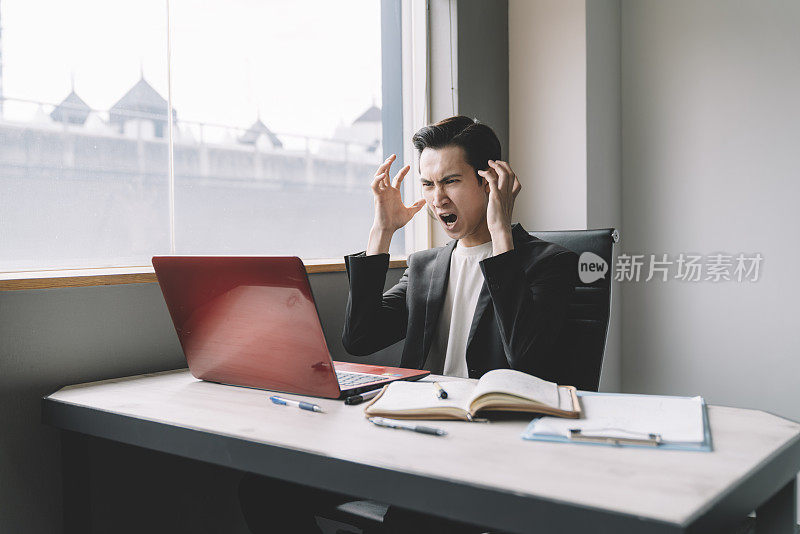 沮丧的年轻亚裔中国商人在办公室盯着笔记本电脑的屏幕举起双手