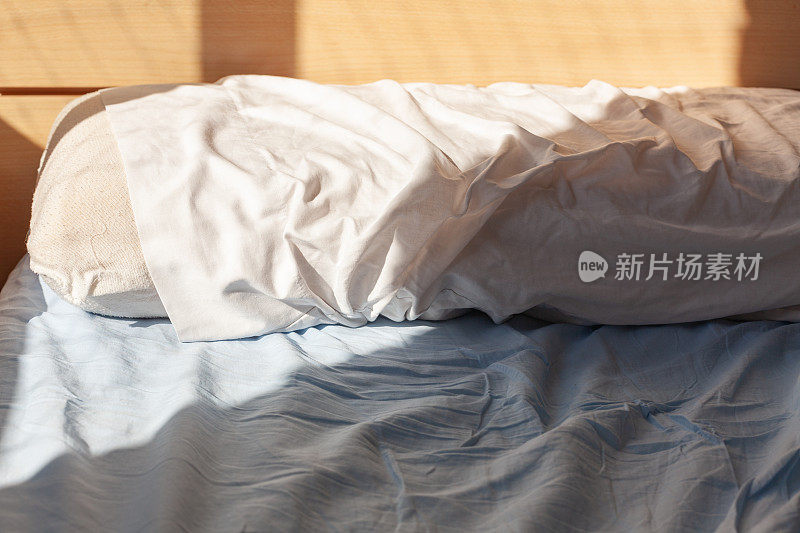 起床概念:枕头放在未整理的床上，床单上有褶皱，晨光照亮