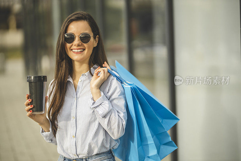 年轻漂亮的女人喝着咖啡，拎着购物袋走路