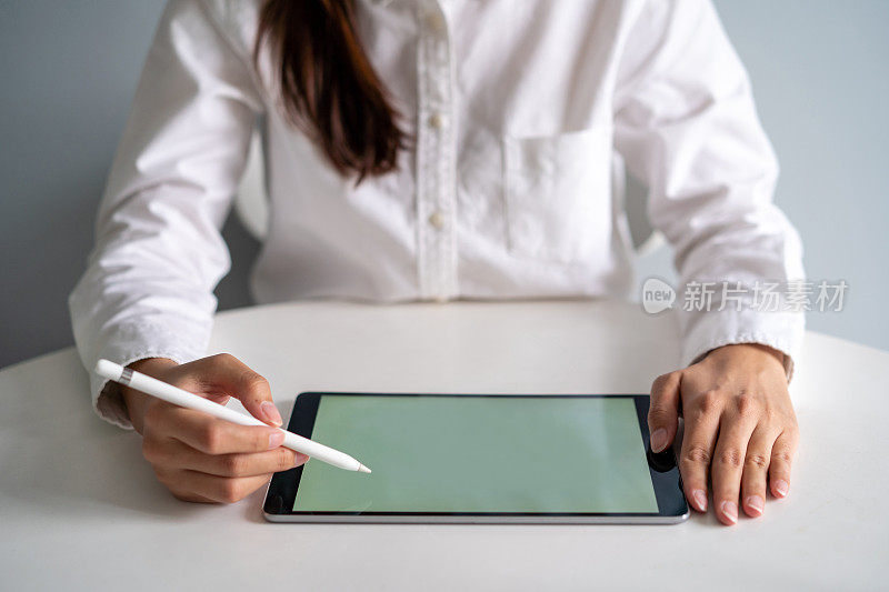 年轻的亚洲女商人在桌子上用数字平板电脑和触控笔工作