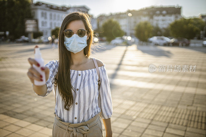 一名年轻女子戴着外科口罩，手上涂着洗手液，在封锁期间站在空荡荡的城镇广场上