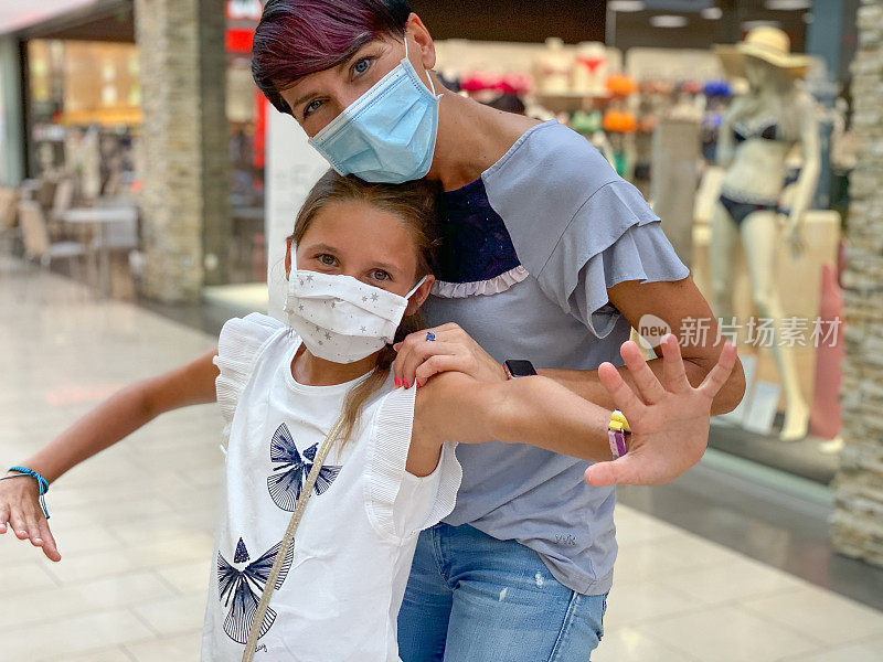 顽皮的女孩在保护面罩吸引注意保持六英尺的距离，而在购物中心与母亲-库存照片
