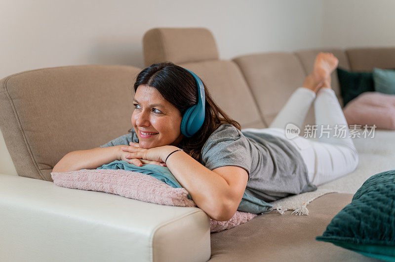 一位成年妇女躺在客厅沙发上的垫子上，戴着耳机