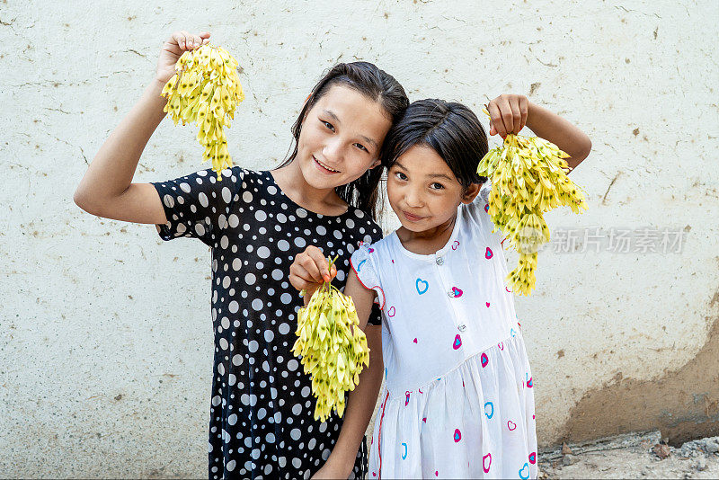 两个女孩拿着金色的叶子，对着镜头微笑