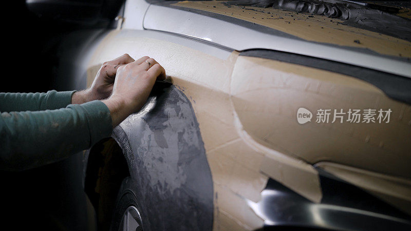 男建设者在汽车维修车间从造型泥中制作细节原型，覆盖车身