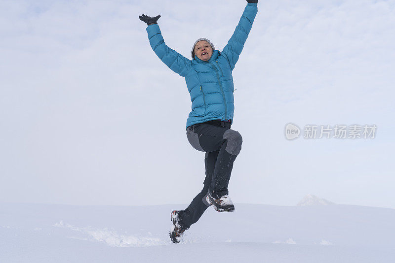 成熟的女人穿着皮大衣在雪地上跳起来