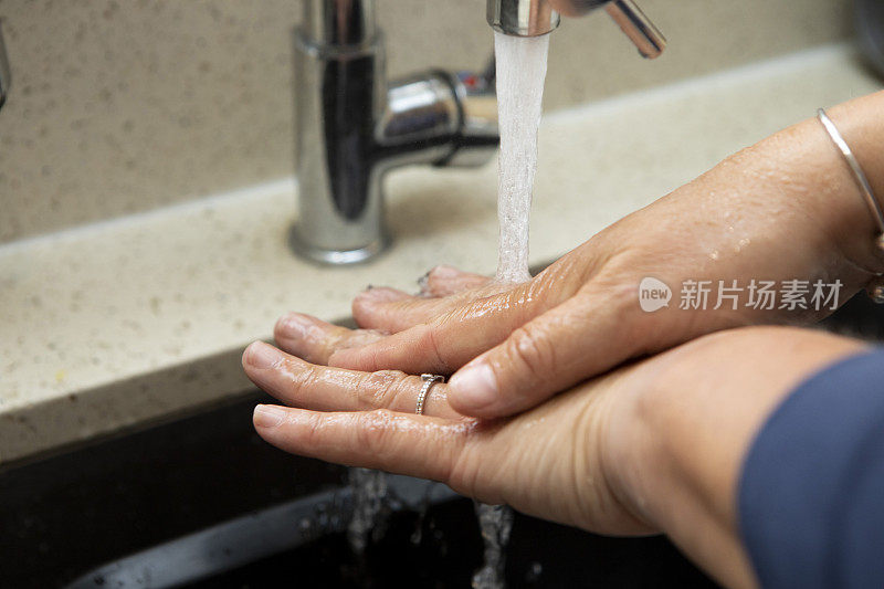 一个女人的手正在厨房水槽的自来水下清洗的特写