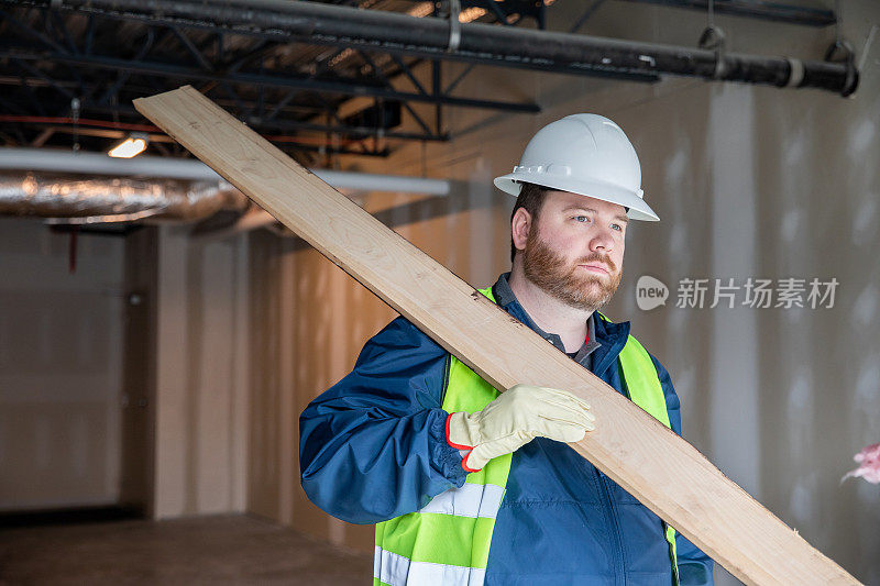 建筑工人或工程师在工地上搬运材料并查看剪贴板上的平面图