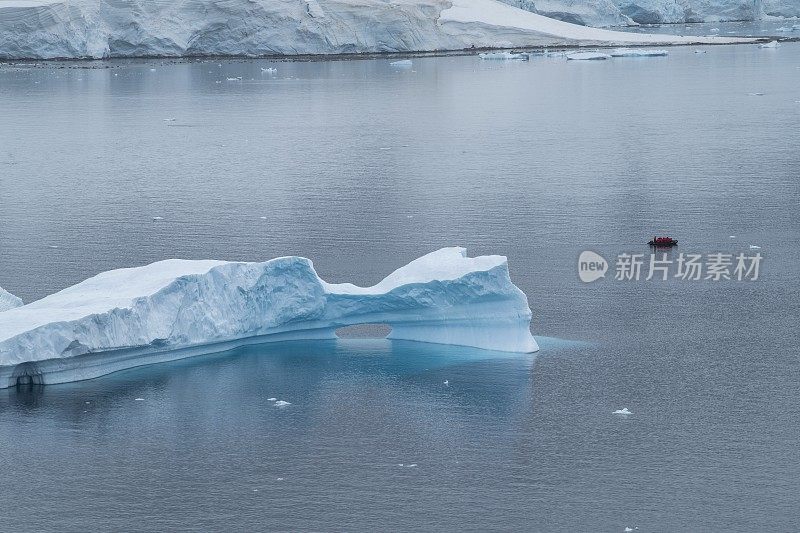 一艘Zodiac橡胶摩托艇载着一艘探险游轮上的乘客，驶过一座有拱门的大冰山