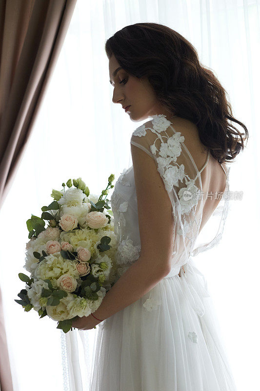 新娘的早晨。一个美丽的女人正在准备一场婚礼，自然的妆容和别致的发型。白色睡衣和结婚礼服