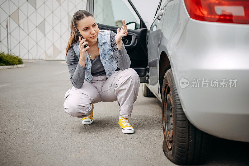 一名妇女看着自己的汽车轮胎漏气，用手机求助