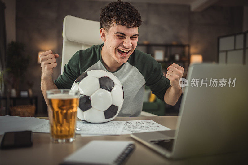 一个十几岁的孩子在课间休息，坐在书桌前用笔记本电脑看足球比赛