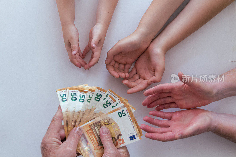 年迈的祖父或祖母双手将50欧元钞票递给他的妻子、丈夫和孙子孙女的另一双手