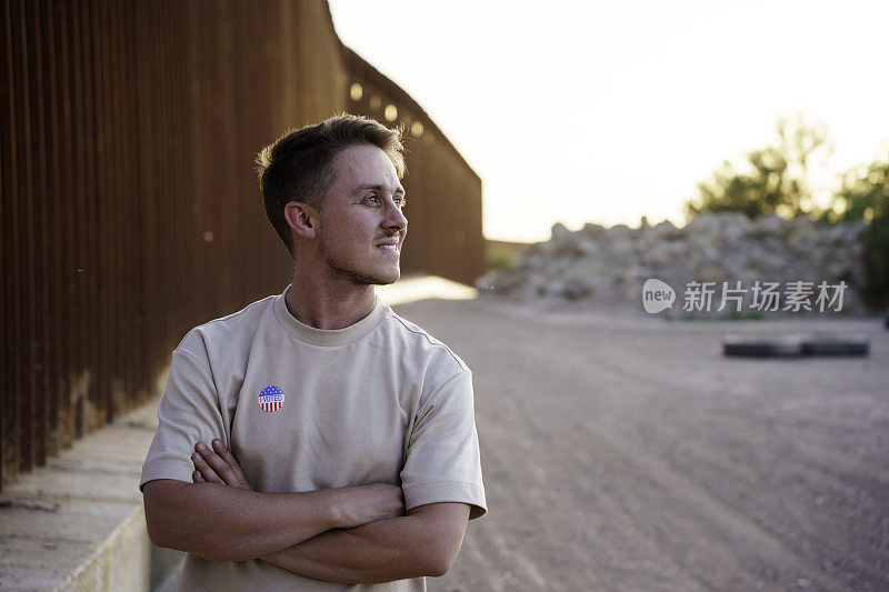 黄昏时分，一名年轻人站在美国德克萨斯州和墨西哥奇瓦瓦州华雷斯之间的国际边境墙前，身上贴着“我投了美国票”的贴纸