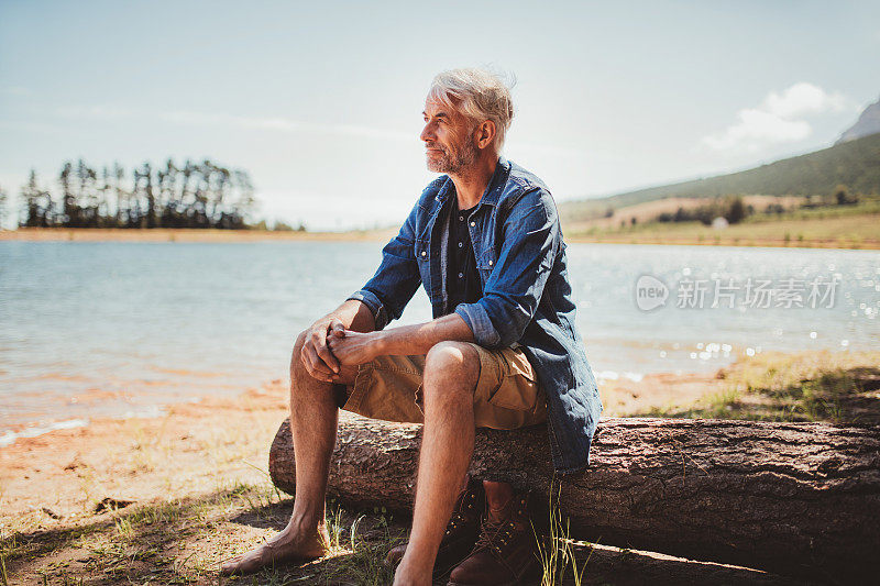 一个成熟的男人坐在湖边的原木上